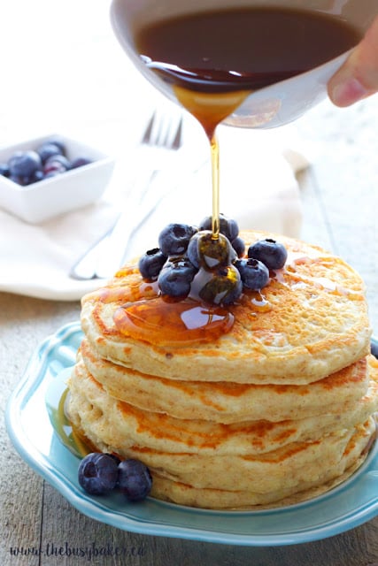 pouring maple syrup onto a stack of homemade buttermilk pancakes