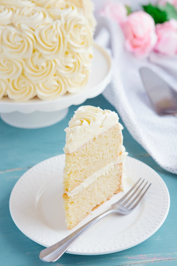 Best Ever Vanilla Bean White Cake slice on white plate with fork and flowers