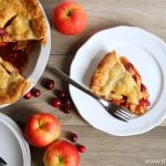 a slice of cranberry apple pie on a white dessert plate with a fork. The rest of the pie sits next to it