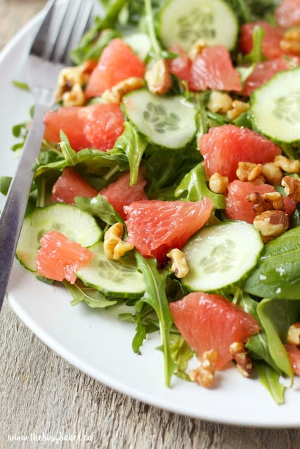 plate of healthy salad made with cucumbers, grapefruit, chopped walnuts, arugula and baby spinach