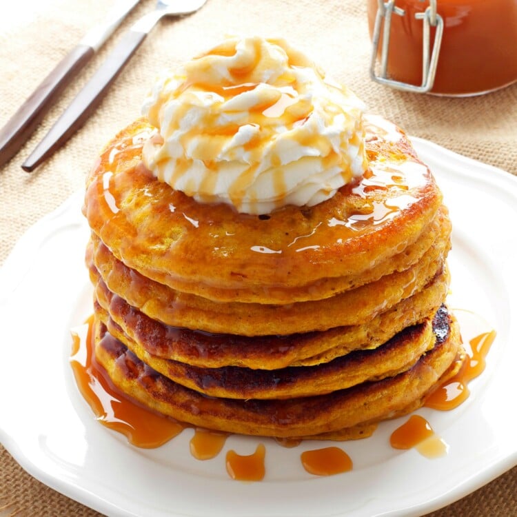 stack of pumpkin pancakes topped with whipped cream and drizzle