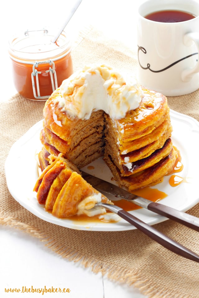 stack of pancakes with a piece cut out of it. a fork and knife resting on the white plate.