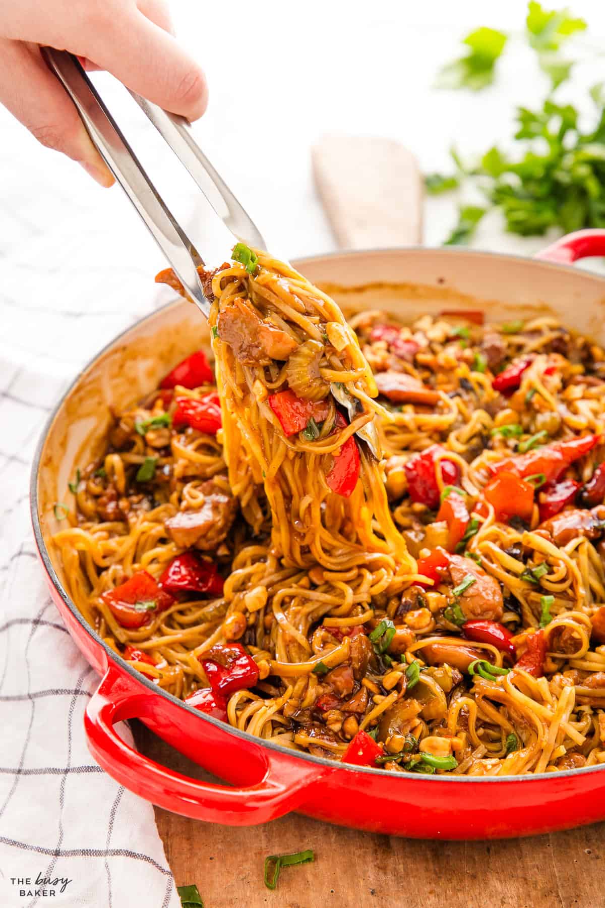 tongs serving kung pao chicken from a red cast iron pan