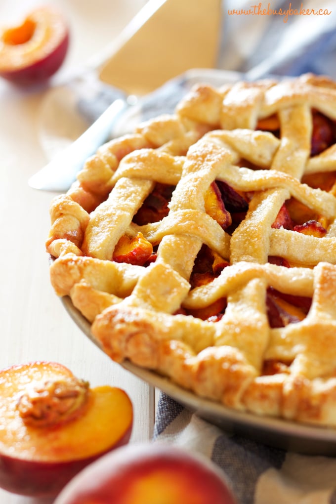 close up image: golden brown crust of the peach pie filling. peaches in the foreground