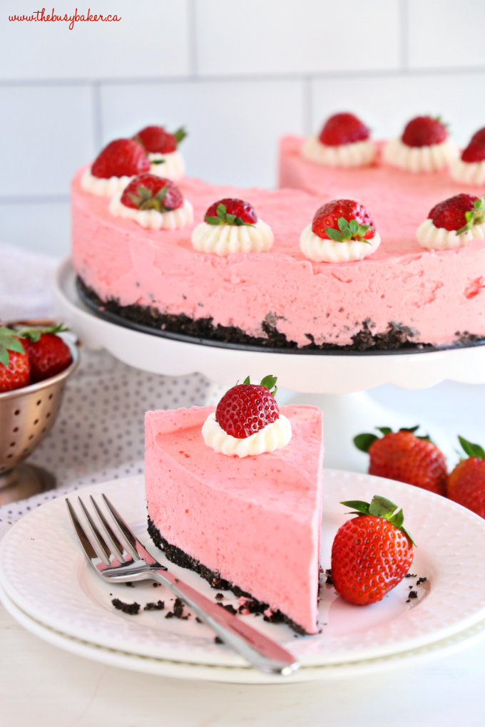 Slice of Easy No Bake Strawberry Cheesecake on white plate with fork and cake on cake stand