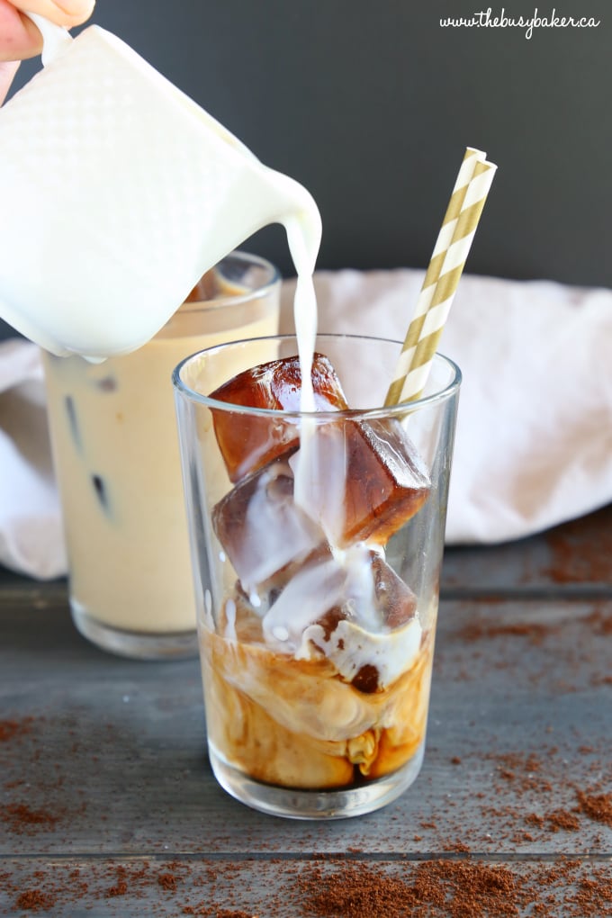 Pouring milk into iced coffee over ice cubes with straws