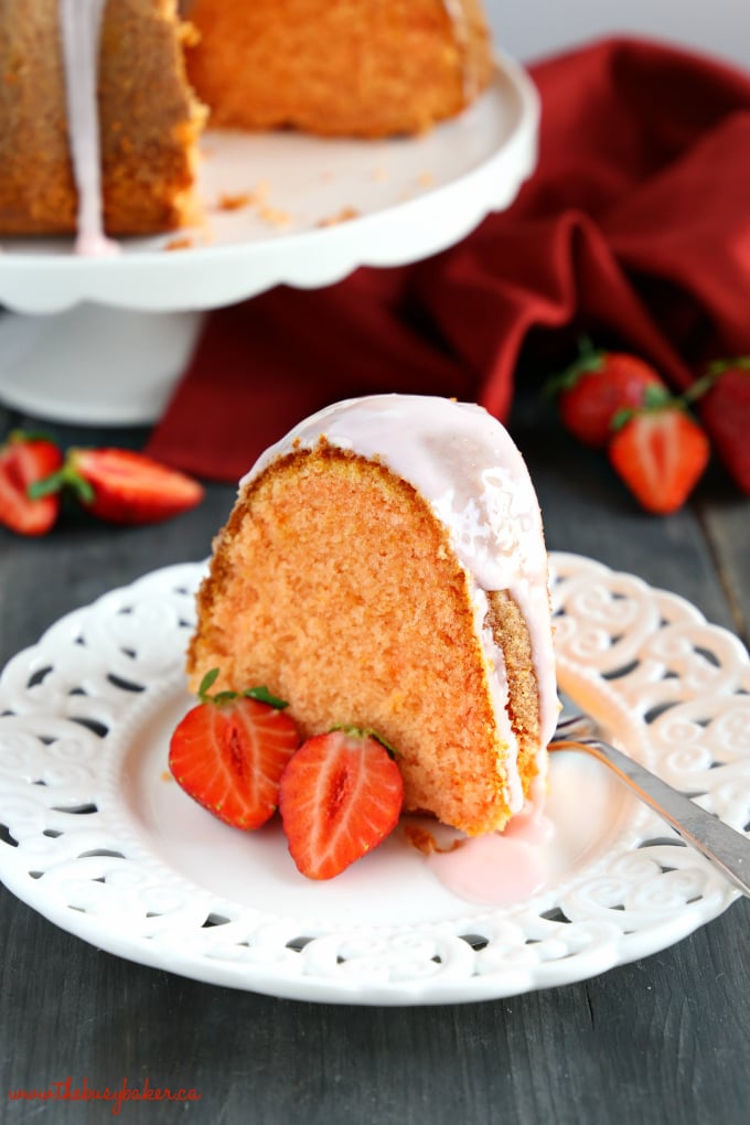 Best Ever Strawberry Pudding Cake dessert on white lace plate with strawberries cut in half