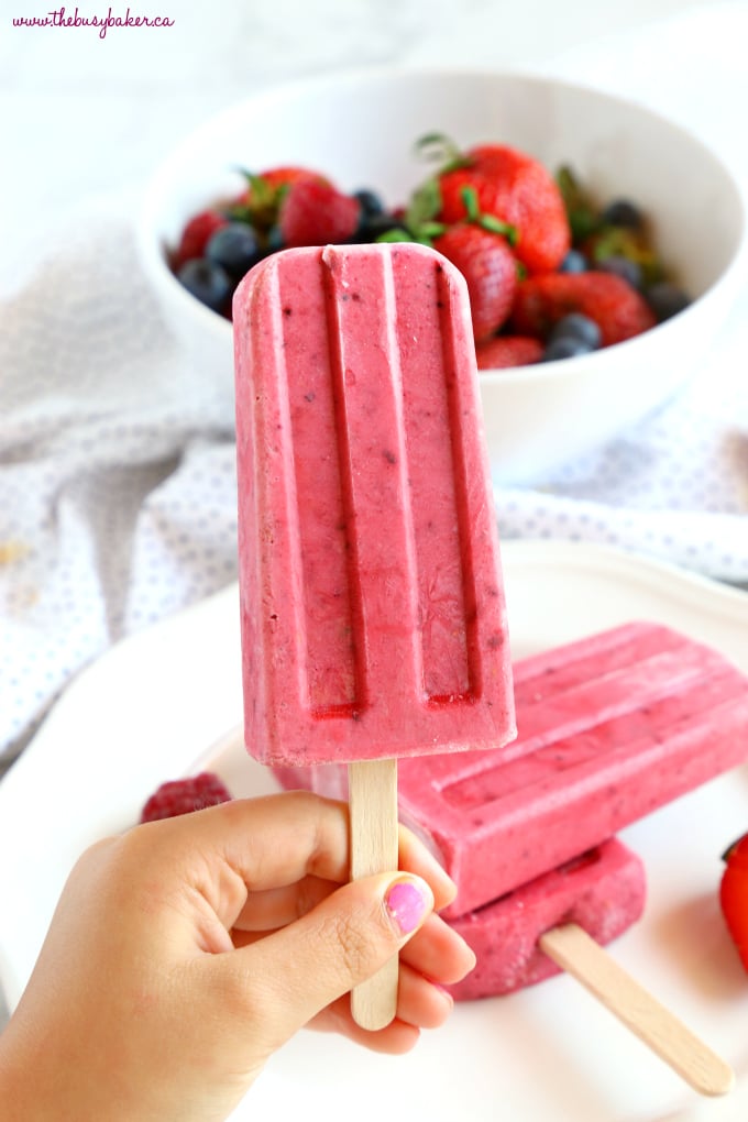 Child's hand holding Healthy Berry Coconut Popsicles with fresh berries