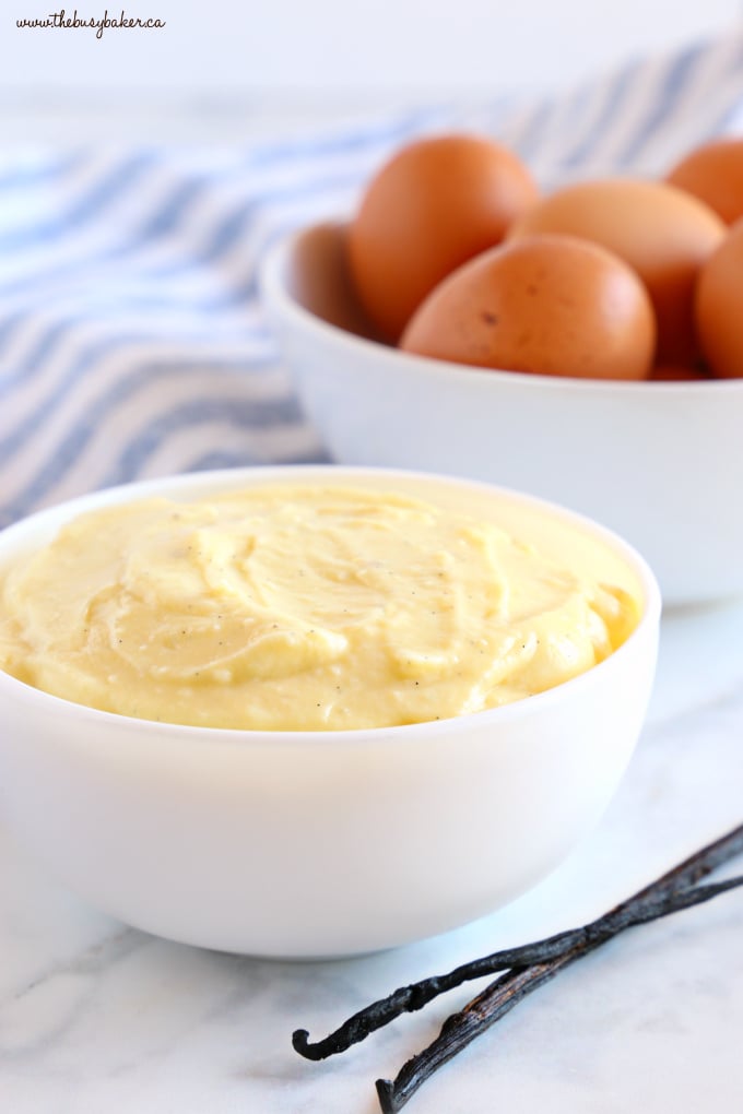 Easy Homemade Vanilla Bean Pastry Cream in white bowl with eggs and blue cloth and vanilla beans