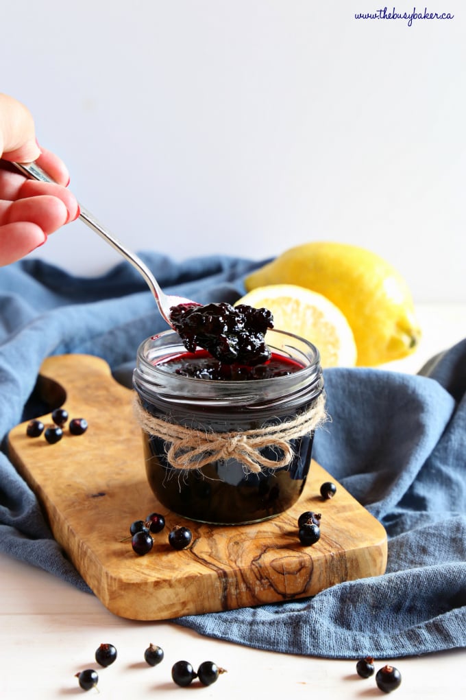 Best Ever Black Currant Jam in mason jar with lemons and spoon