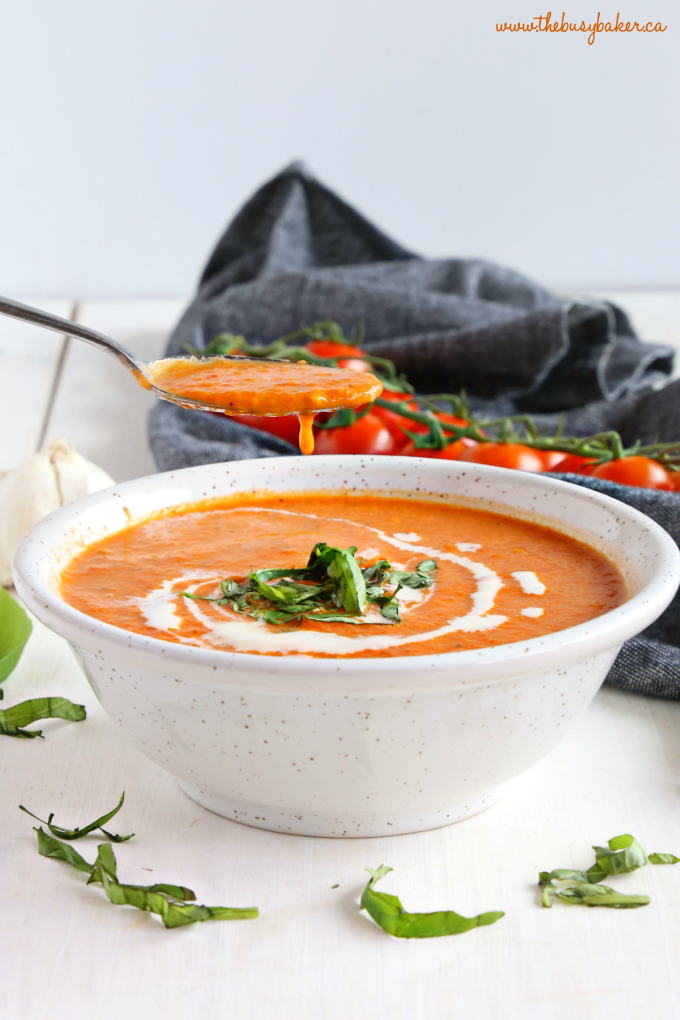 Easy Homemade Roasted Tomato Soup on spoon with white bowl and basil ribbons