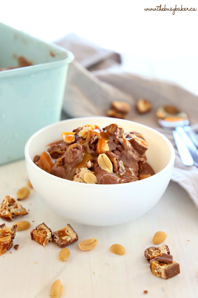 Easy No Churn Snickers Ice Cream in white bowl with snickers bars chunks and peanuts