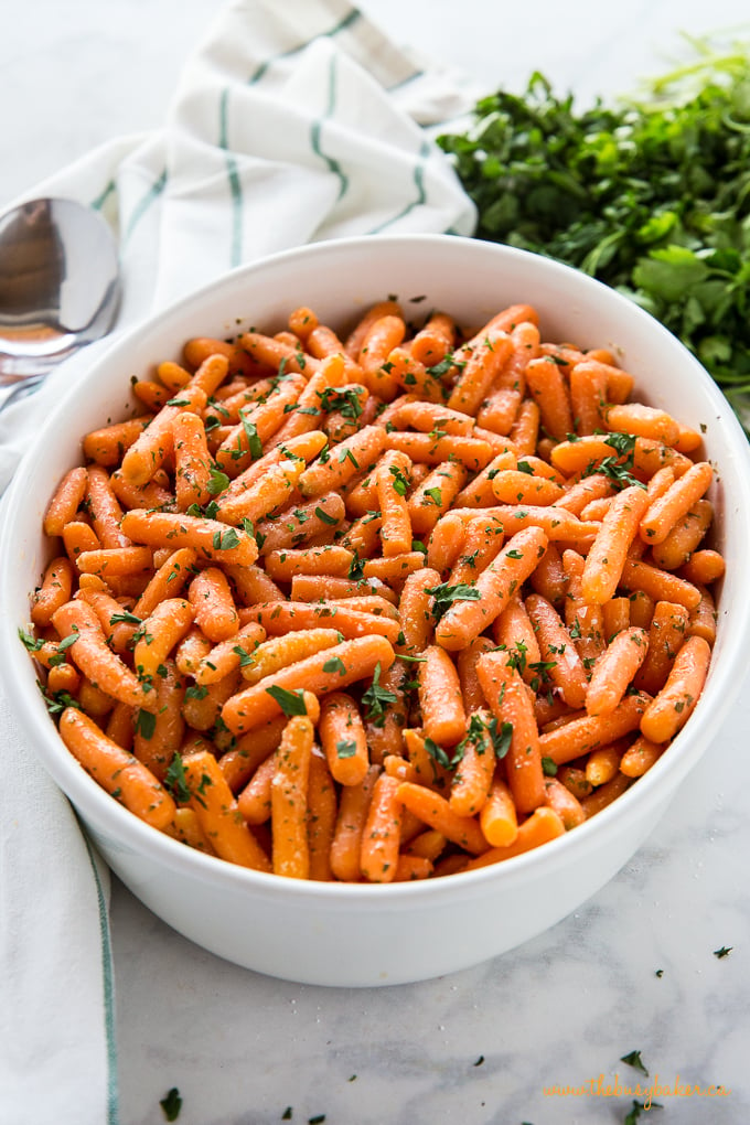 Garlic Butter Roasted Carrots in white oval baking dish with green parsley