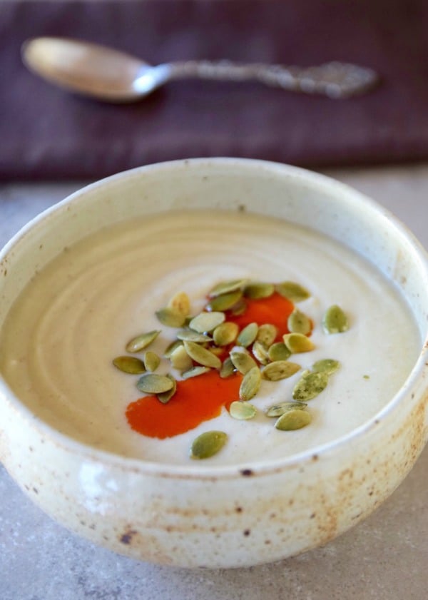 bowl of roasted cauliflower soup garnished with chili oil and pepitas