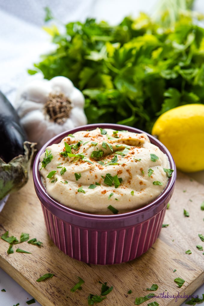 Easy Homemade Baba Ganoush in purple bowl with fresh herbs, garlic and lemon