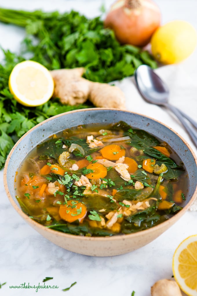 Crock Pot Lemon Ginger Chicken Soup in blue pottery bowl with fresh herbs and lemon