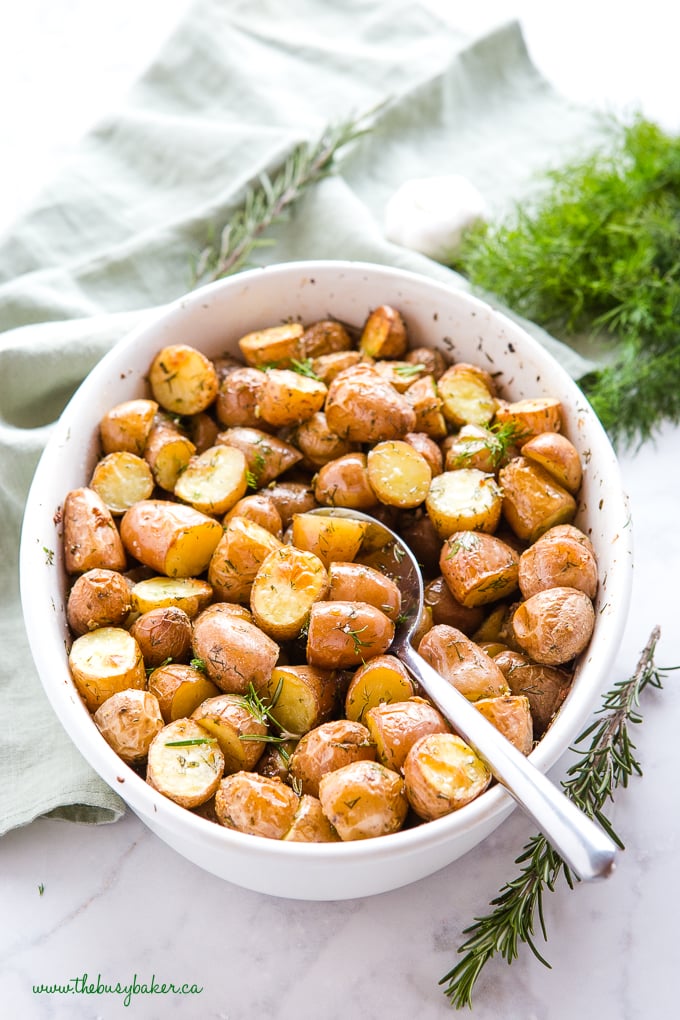 Rosemary Dill Roasted Potatoes in white dish with a spoon and fresh herbs
