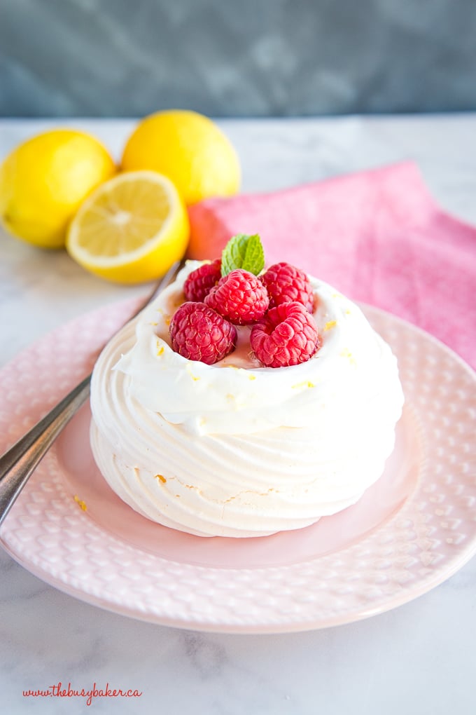 Lemon Raspberry Meringue Nests with fresh raspberries, lemon whipped cream on pink plate with gold fork