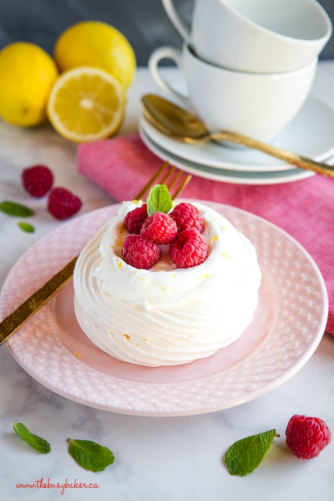 Lemon Raspberry Meringue Nests with fresh raspberries, lemon whipped cream on pink plate with gold fork