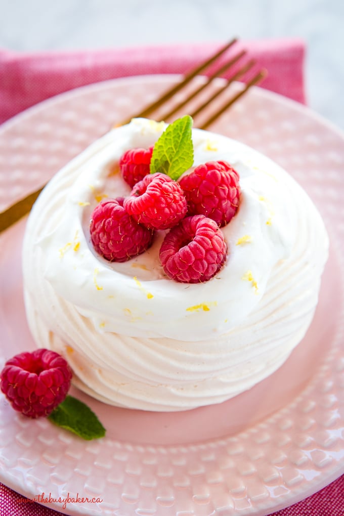 Lemon Raspberry Meringue Nests with fresh raspberries, lemon whipped cream on pink plate with gold fork