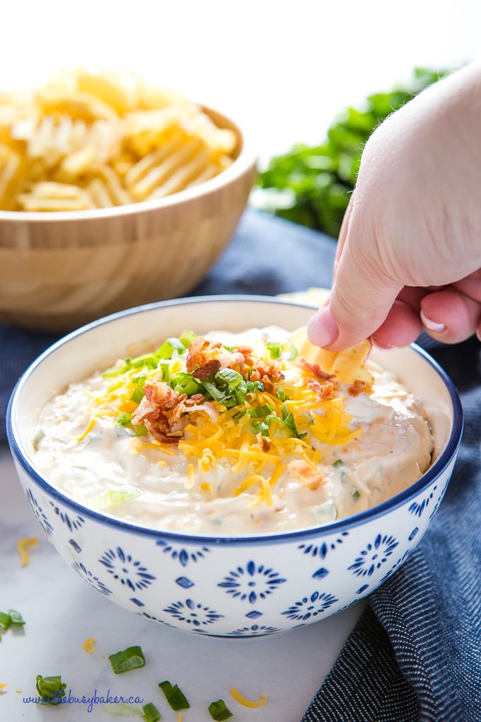 hand dipping chip into bowl of ranch dip with bacon and cheddar