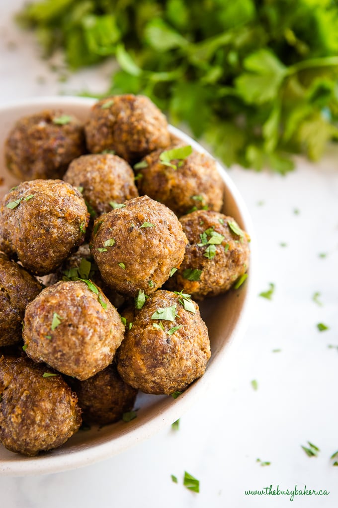 close up photo of meatballs in bowl with green herbs