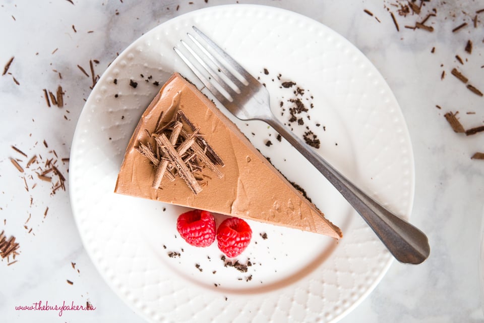 chocolate cheesecake on white plate with shaved chocolate and raspberries