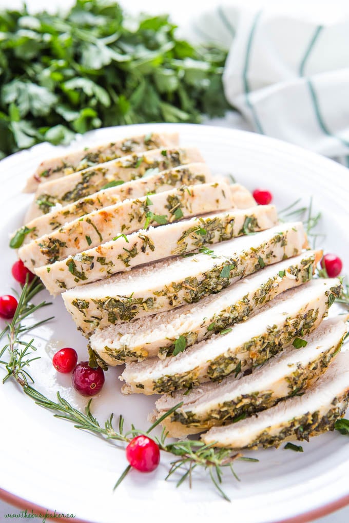 sliced roast turkey breast on white terra cotta plate with cranberries and rosemary