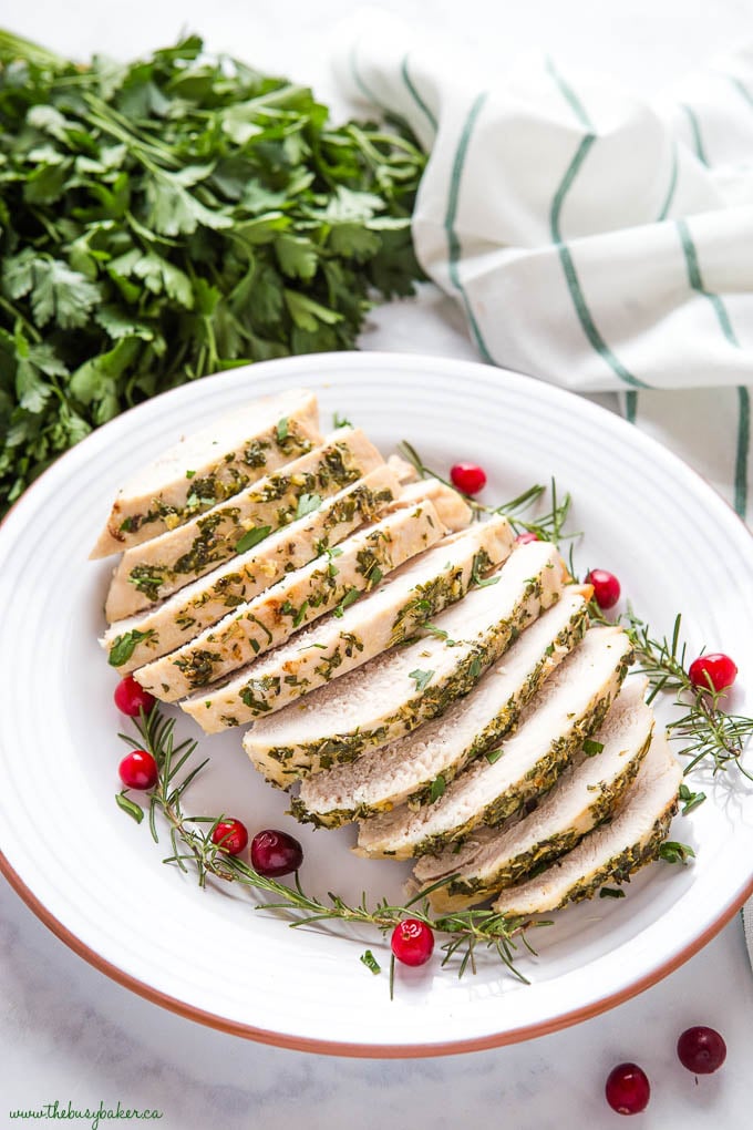 slices of roast turkey on plate with fresh herbs and cranberries