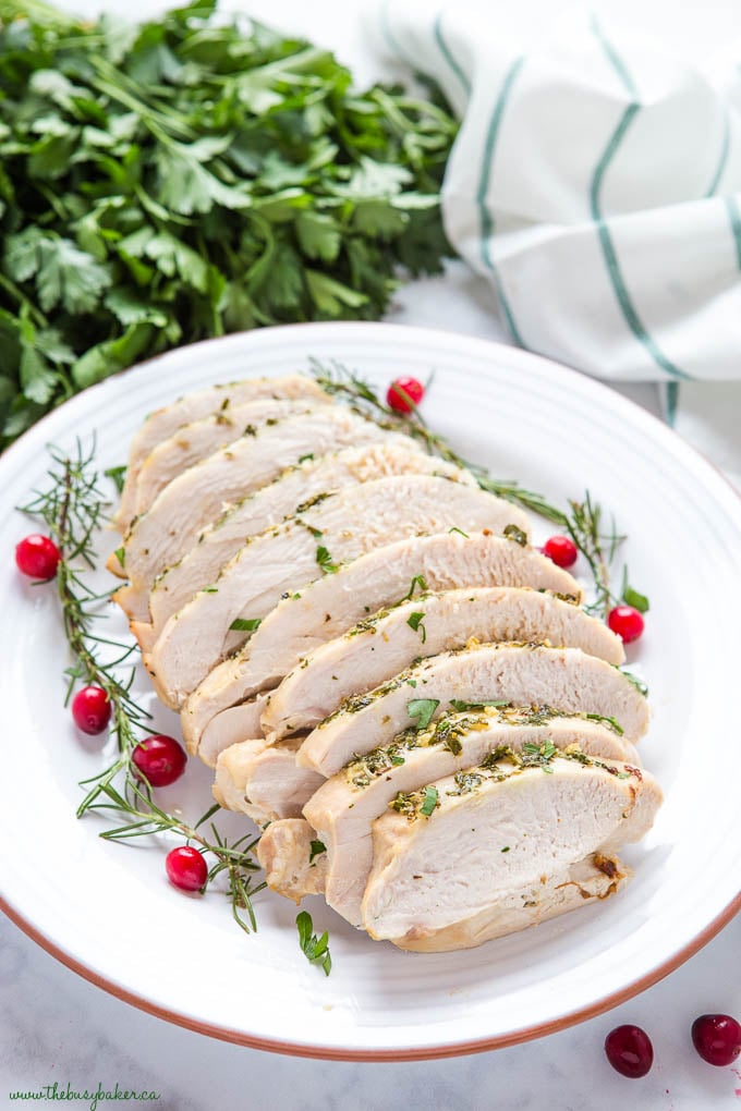 garlic herb roasted boneless skinless turkey breast on white plate with whole cranberries and fresh rosemary