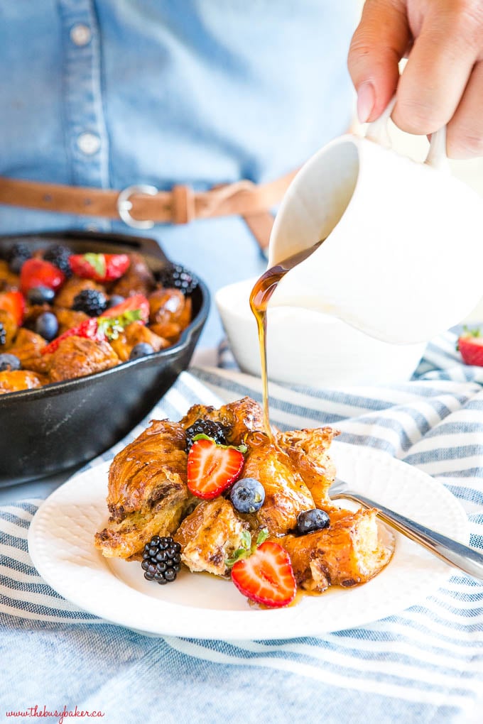 woman pouring syrup onto baked croissant French toast with berries
