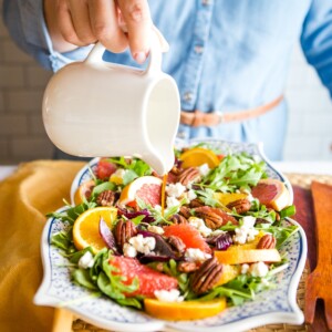 pouring dressing onto a spinach arugula salad in large bowl