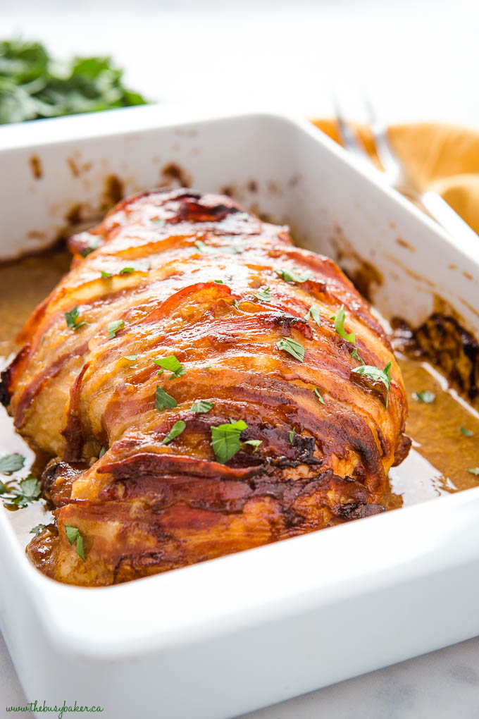 bacon wrapped dijon roast turkey breast in white pan with juices