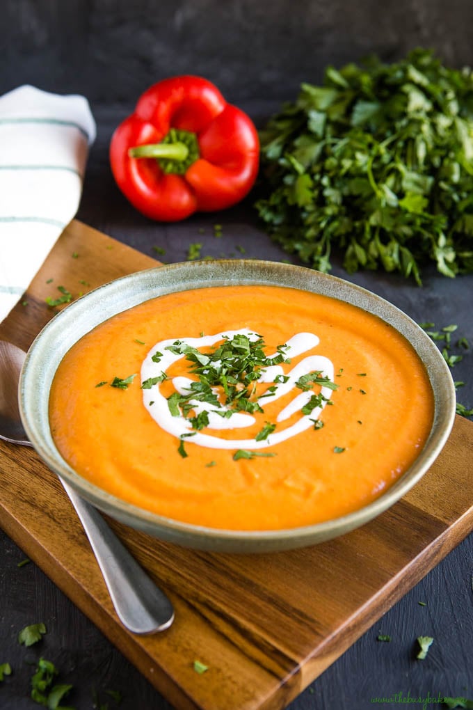 roasted red peppers cauliflower soup in green pottery bowl garnished with coconut cream and parsley