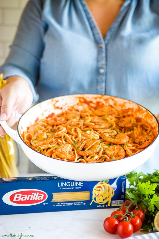woman serving seafood marinara linguine in white cast iron pan