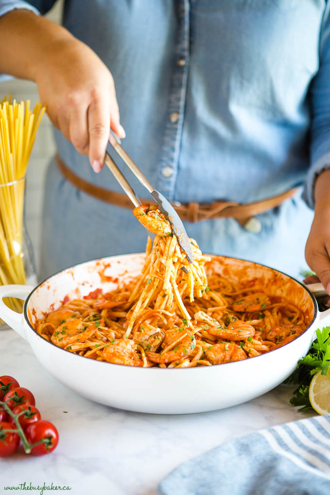 woman serving seafood marinara linguine in white cast iron skillet