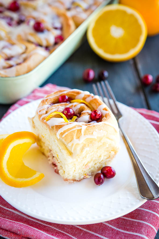 sweet roll on white plate with orange and cranberries