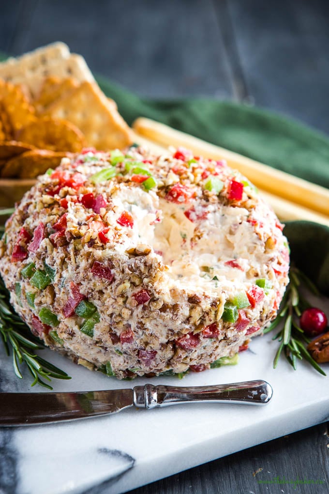 soft cheddar cheese ball covered with red and green peppers on a cheese board