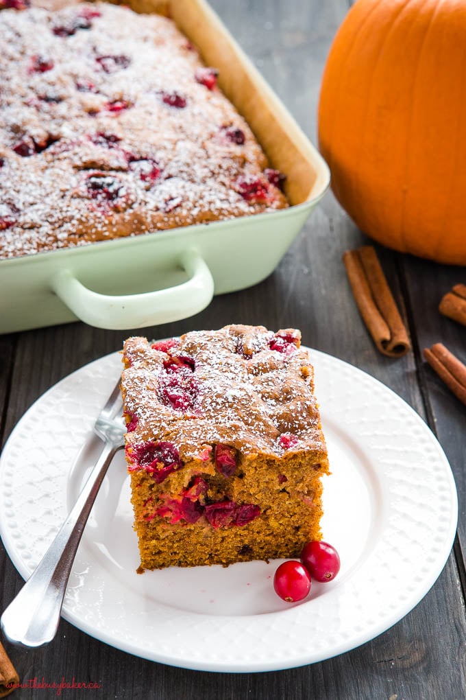 easy pumpkin cranberry cake, sliced on white plate with fresh cranberries and powdered sugar