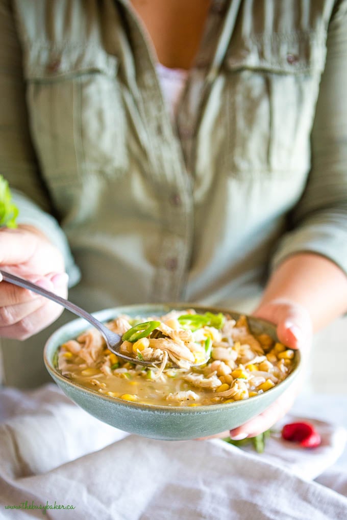 woman holding spoonful of white chicken chili in green bowl