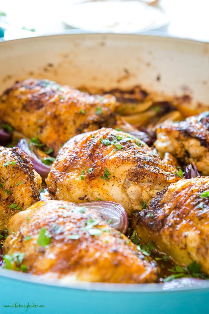 African chicken thighs in blue pan with slices of red onion