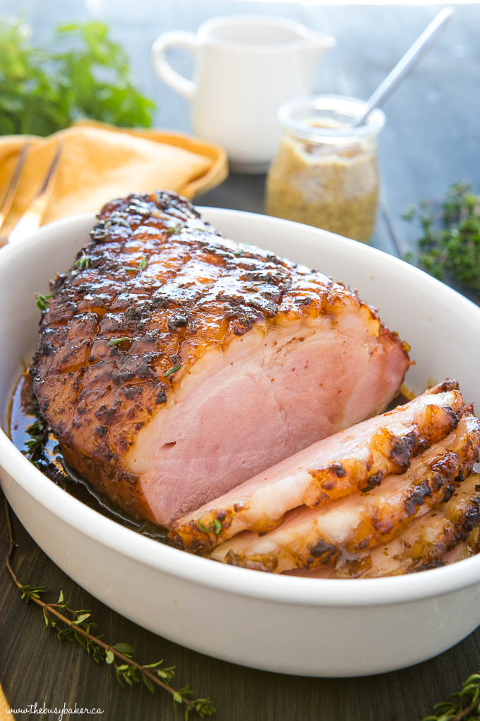 holiday ham baked with a sticky maple glaze cut into slices in a white serving dish