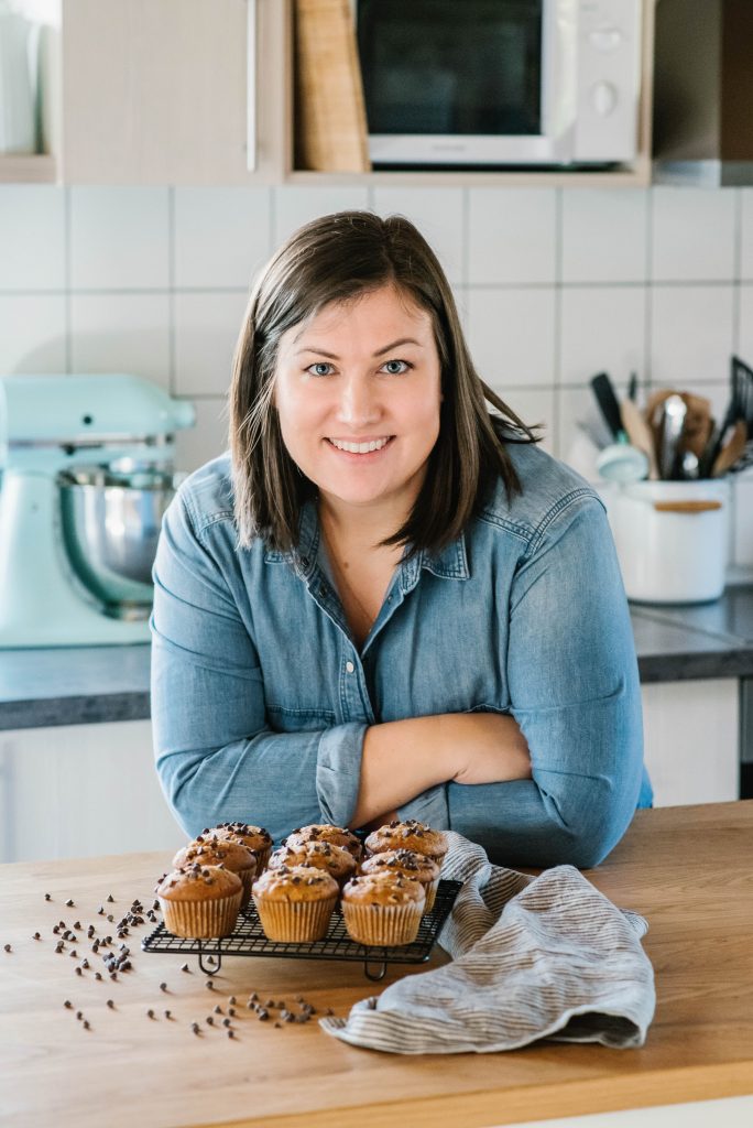 woman in kitchen with batch of homemade chocolate chip muffins