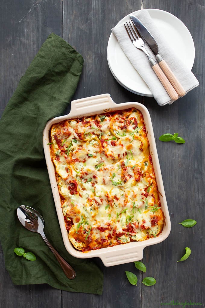 ricotta stuffed shells pasta bake next to stack of white dinner plate, fork, knife, and white napkin