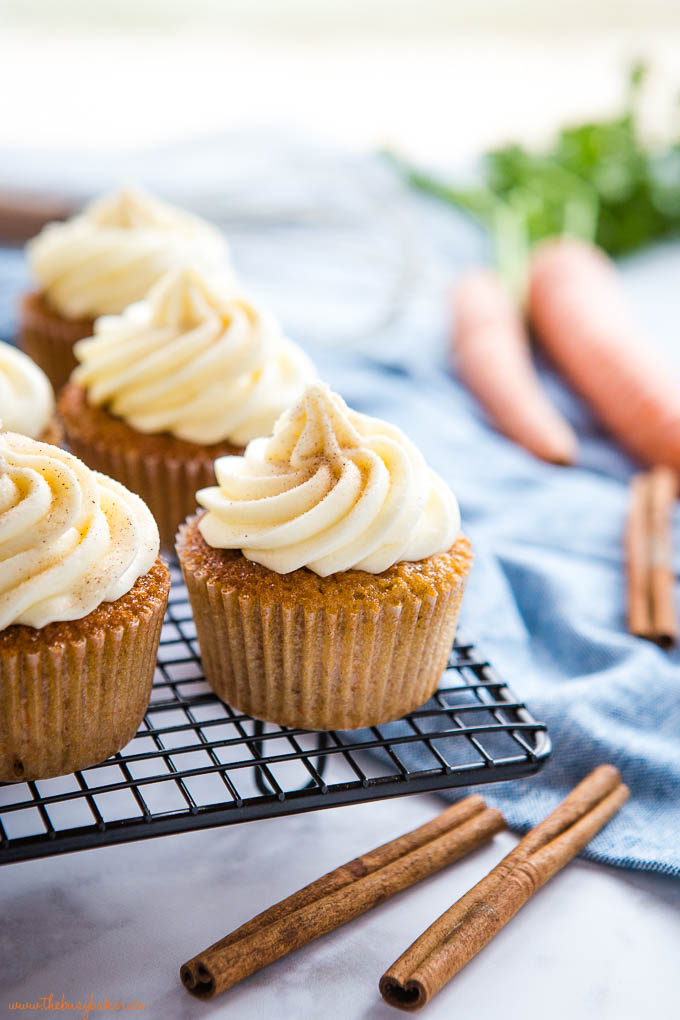 carrot cake cupcakes on wire rack with cream cheese frosting and cinnamon sticks