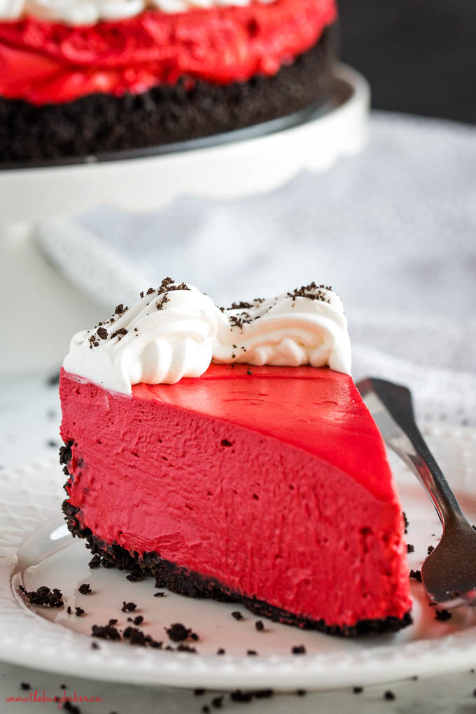 slice of creamy red cheesecake with chocolate cookie crust on white plate with whipped cream