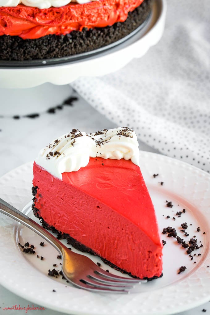 slice of creamy red cheesecake with chocolate cookie crust on white plate