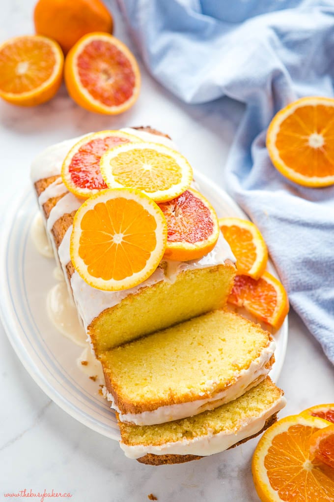 overhead photo: moist loaf cake with orange glaze and fresh orange slices on white platter