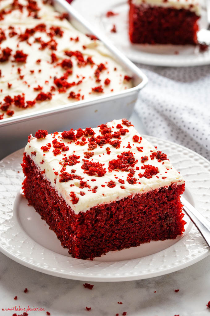 square of red sheet cake topped with cream cheese buttercream frosting on a white plate