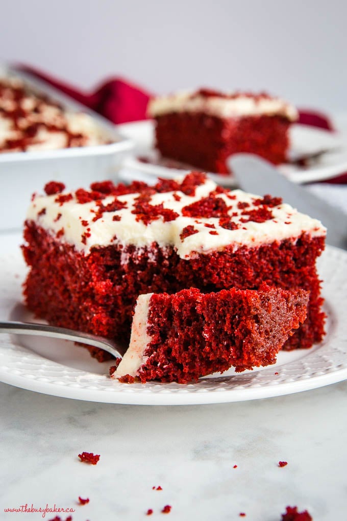 slice of red velvet cake on white plate with bite on fork